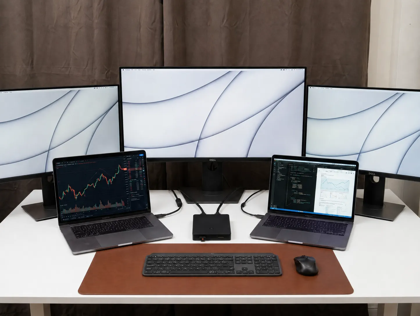 A desk with three monitors and two laptops, one keyboard and one mouse, and the MousePass unit sitting between the two laptops with USB cables running to each